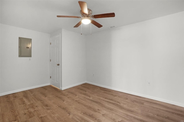 empty room featuring visible vents, ceiling fan, baseboards, electric panel, and wood finished floors