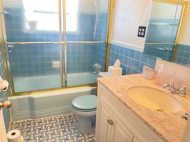 bathroom with bath / shower combo with glass door, toilet, a wainscoted wall, vanity, and tile walls