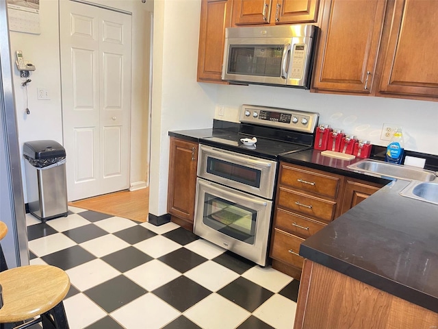 kitchen featuring dark countertops, light floors, stainless steel appliances, and brown cabinetry