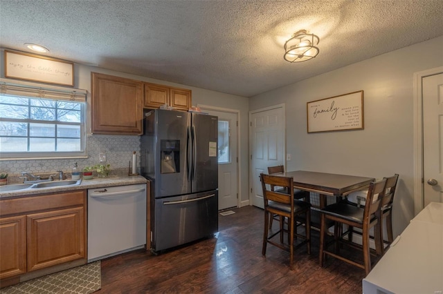 kitchen with dark wood-type flooring, a sink, stainless steel fridge with ice dispenser, decorative backsplash, and dishwasher