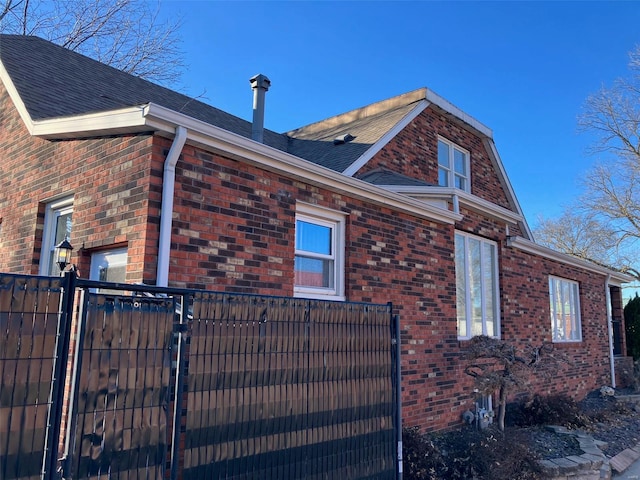 view of side of home with brick siding, a shingled roof, and fence