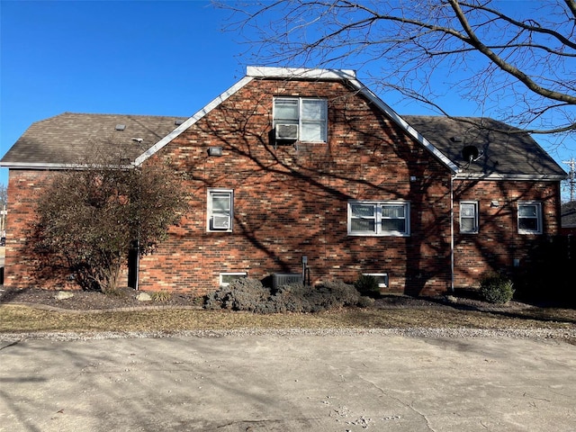 view of side of property featuring brick siding, a gambrel roof, and a shingled roof