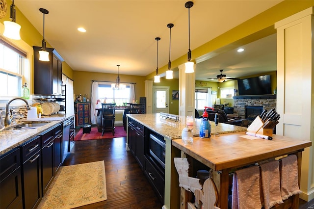 kitchen featuring a center island, dark wood finished floors, ceiling fan with notable chandelier, a fireplace, and a sink