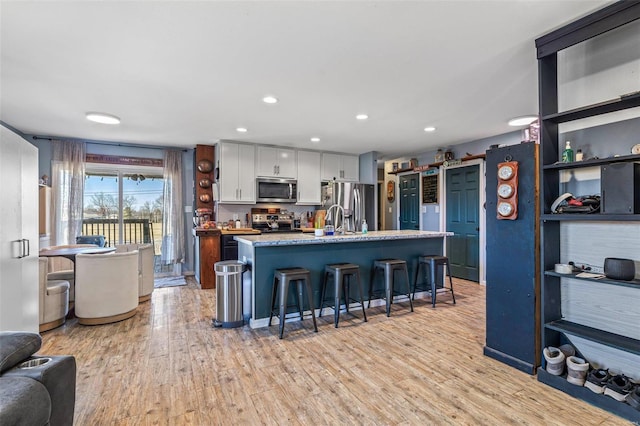 kitchen with light wood-style flooring, a kitchen island with sink, a breakfast bar area, and stainless steel appliances