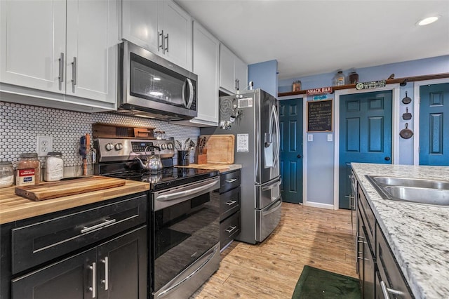 kitchen featuring butcher block countertops, a sink, stainless steel appliances, light wood-type flooring, and backsplash