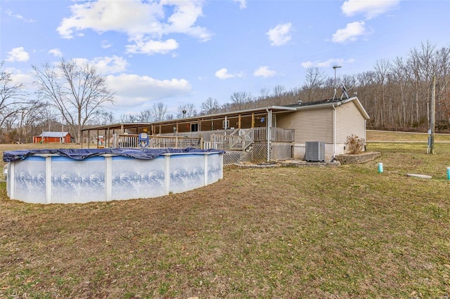 view of swimming pool featuring a covered pool, a lawn, a deck, and central AC unit