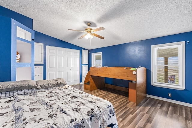 bedroom featuring lofted ceiling, a closet, a textured ceiling, wood finished floors, and baseboards