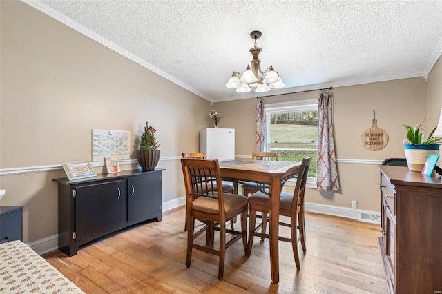 dining room featuring a chandelier, light wood finished floors, a textured ceiling, and ornamental molding