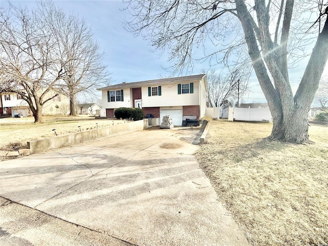 bi-level home with a garage, concrete driveway, brick siding, and fence