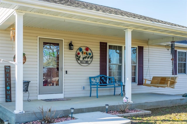 entrance to property featuring a porch and a shingled roof