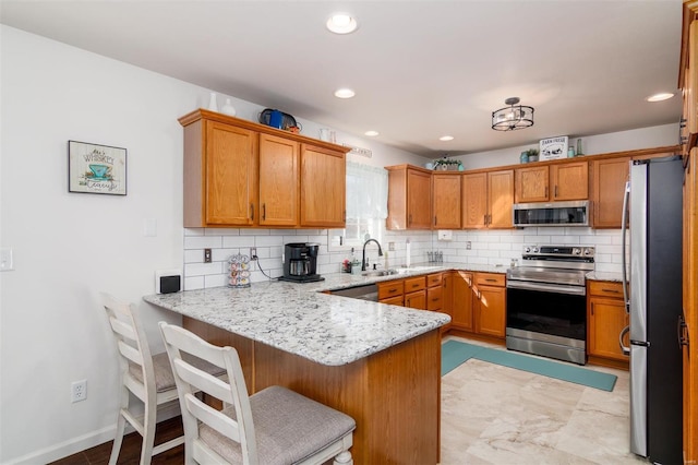 kitchen featuring light stone countertops, decorative backsplash, a peninsula, stainless steel appliances, and a sink