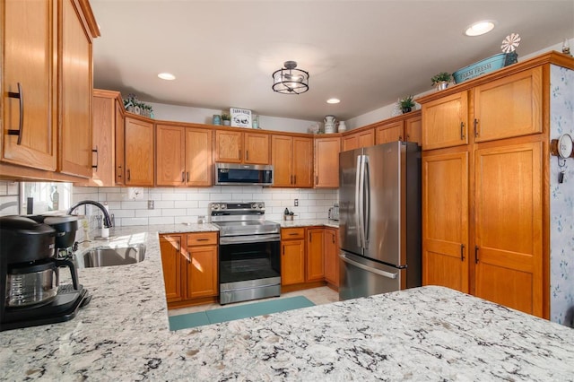 kitchen featuring light stone counters, a sink, stainless steel appliances, tasteful backsplash, and brown cabinets