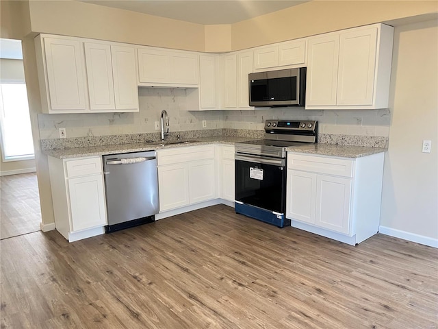 kitchen featuring a sink, white cabinetry, appliances with stainless steel finishes, light wood-type flooring, and decorative backsplash