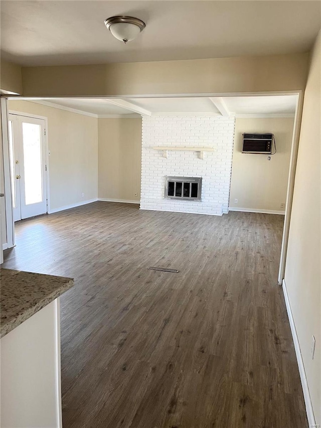 unfurnished living room featuring a brick fireplace, baseboards, dark wood-style floors, and an AC wall unit