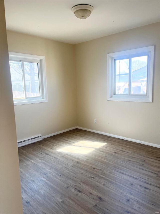 spare room with a baseboard heating unit, wood finished floors, and baseboards