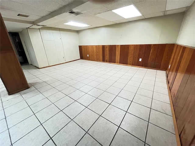 finished basement featuring a paneled ceiling, wainscoting, visible vents, and wooden walls