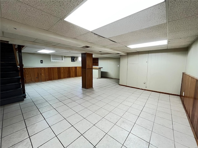 below grade area featuring wooden walls, a drop ceiling, and wainscoting