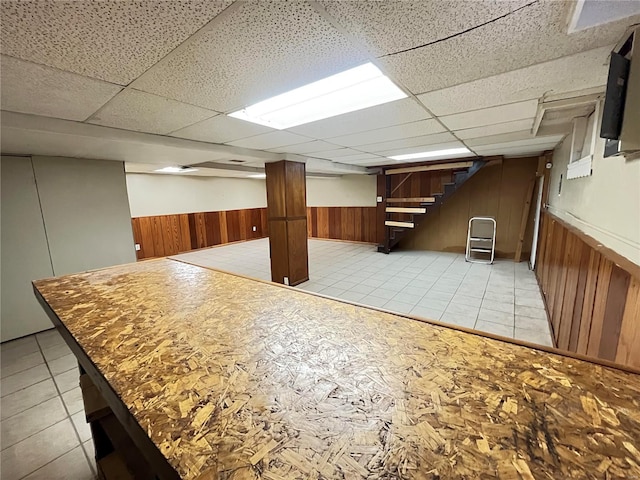 finished basement with a wainscoted wall, wooden walls, and stairway