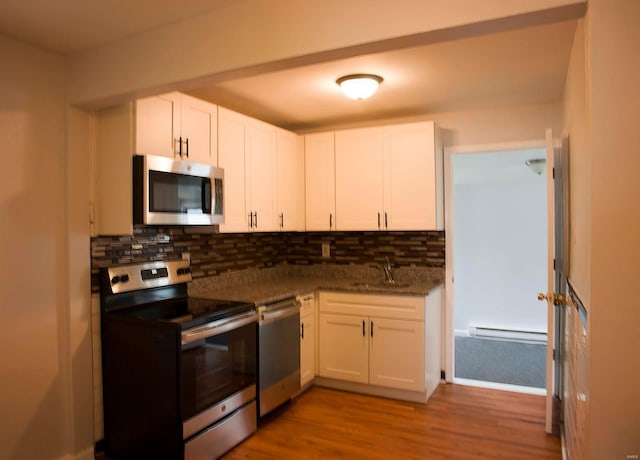 kitchen with tasteful backsplash, baseboard heating, appliances with stainless steel finishes, white cabinets, and a sink