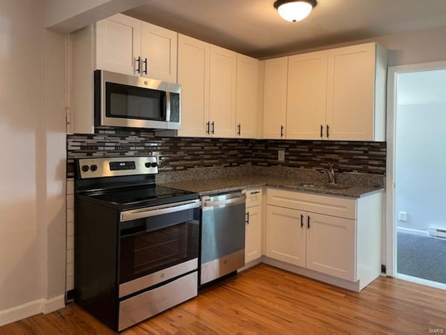 kitchen featuring tasteful backsplash, light wood-type flooring, appliances with stainless steel finishes, white cabinetry, and a sink