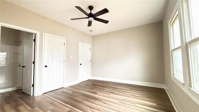 unfurnished bedroom featuring baseboards, multiple windows, wood finished floors, and a ceiling fan