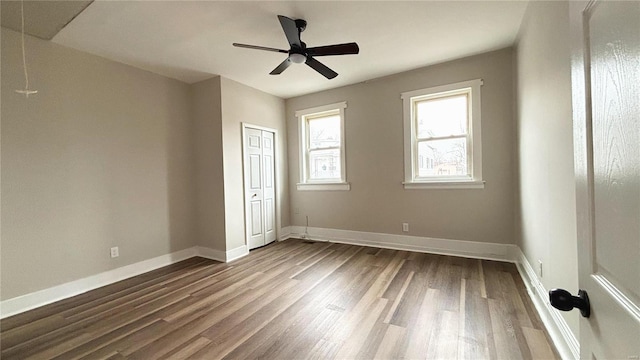 unfurnished bedroom with dark wood-type flooring, ceiling fan, baseboards, attic access, and a closet