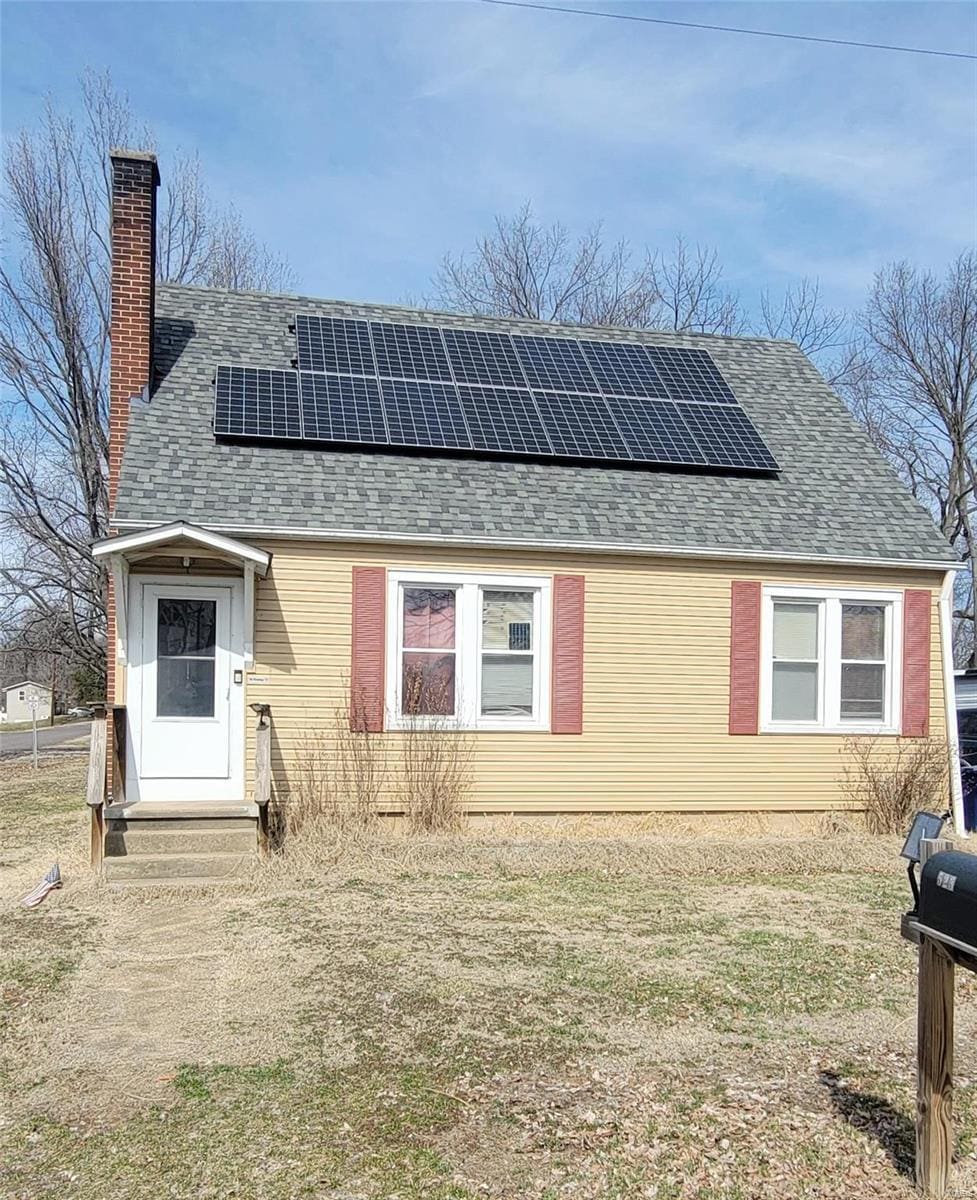 view of front of home featuring entry steps, a shingled roof, a chimney, and solar panels