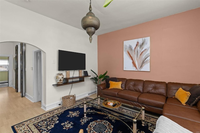 living area featuring light wood-type flooring, arched walkways, and baseboards