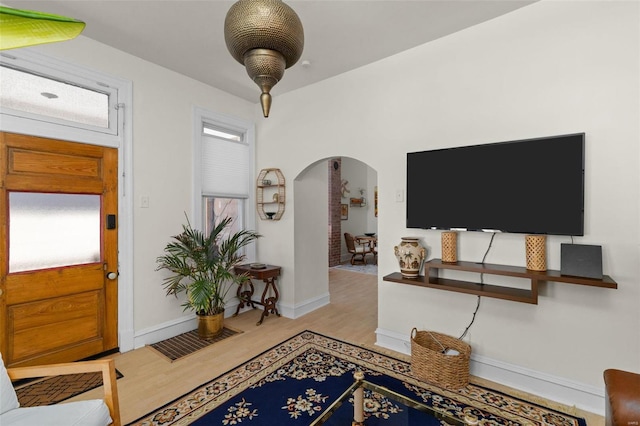 entryway with arched walkways, wood finished floors, and baseboards