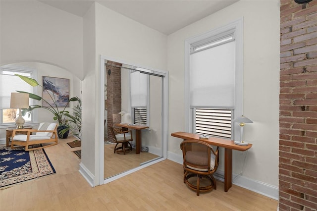 home office featuring brick wall, baseboards, and wood finished floors