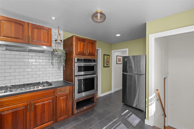 kitchen with decorative backsplash, dark tile patterned flooring, dark countertops, appliances with stainless steel finishes, and under cabinet range hood