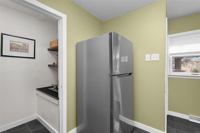 kitchen with freestanding refrigerator, visible vents, dark tile patterned floors, and baseboards