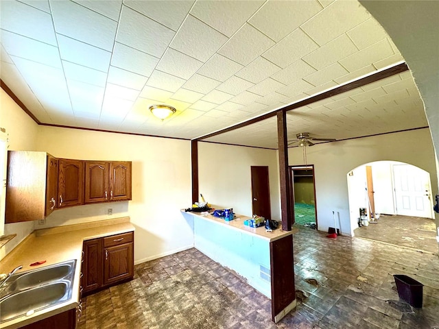 kitchen featuring arched walkways, light countertops, ornamental molding, open floor plan, and a sink