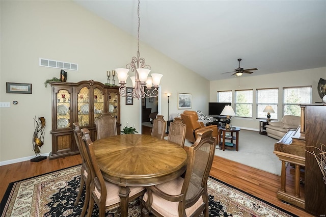 dining area with visible vents, high vaulted ceiling, ceiling fan with notable chandelier, wood finished floors, and baseboards