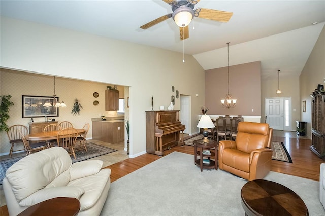 living area featuring high vaulted ceiling, ceiling fan with notable chandelier, wood finished floors, wallpapered walls, and baseboards