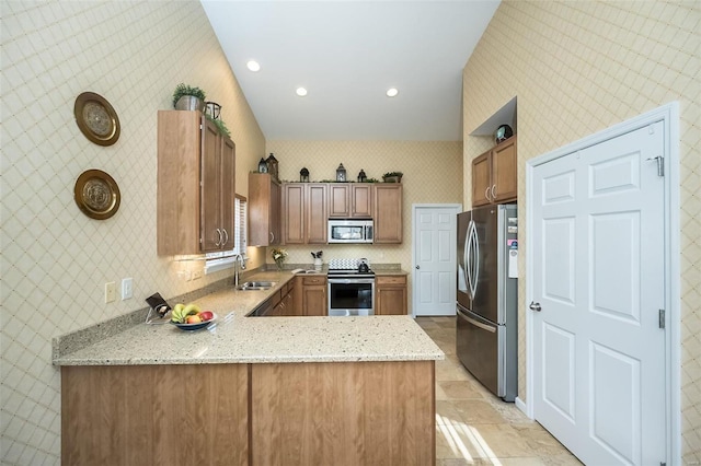 kitchen with a sink, appliances with stainless steel finishes, a peninsula, wallpapered walls, and light stone countertops