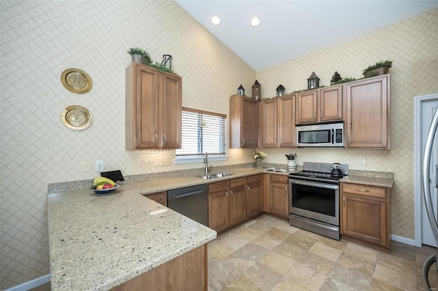 kitchen with a sink, light stone counters, appliances with stainless steel finishes, wallpapered walls, and baseboards