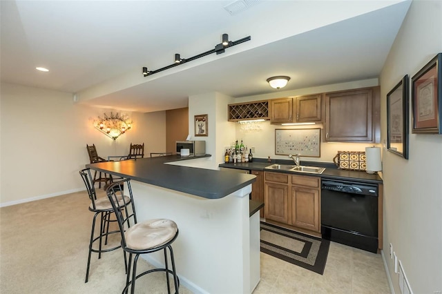 kitchen with visible vents, a sink, black dishwasher, dark countertops, and a breakfast bar area