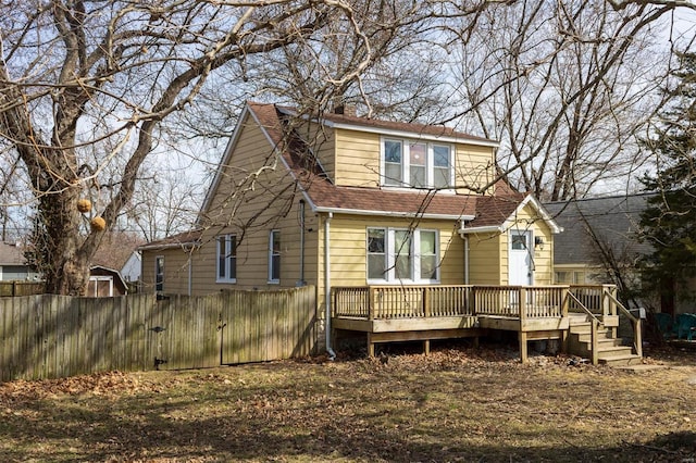 rear view of house featuring a shingled roof, fence, and a deck