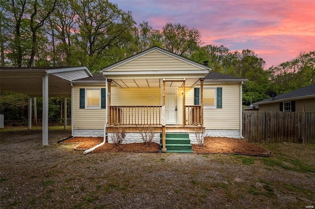 view of front of property featuring covered porch, a carport, a shingled roof, and fence