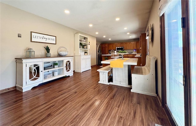 kitchen featuring brown cabinetry, stainless steel microwave, dark wood-type flooring, light countertops, and open shelves