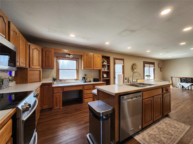 kitchen featuring stainless steel appliances, dark wood-type flooring, a sink, light countertops, and an island with sink