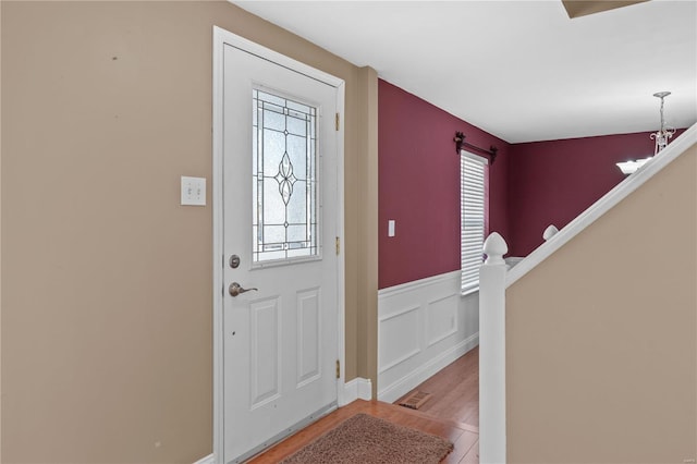 foyer entrance with a wainscoted wall, wood finished floors, visible vents, and a chandelier