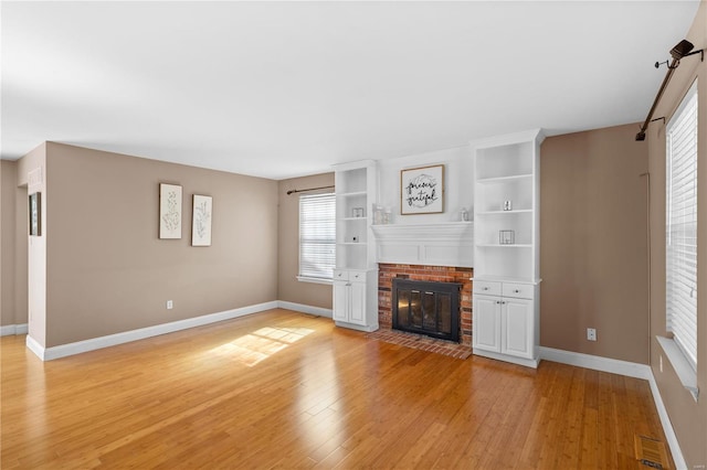 unfurnished living room featuring built in shelves, baseboards, a brick fireplace, and light wood-style flooring