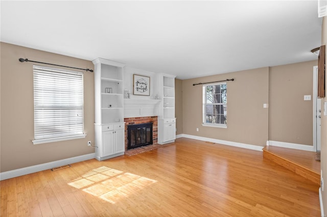 unfurnished living room featuring visible vents, baseboards, a fireplace, and light wood finished floors