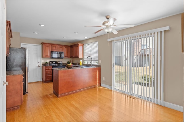 kitchen featuring baseboards, light wood finished floors, a peninsula, ceiling fan, and appliances with stainless steel finishes