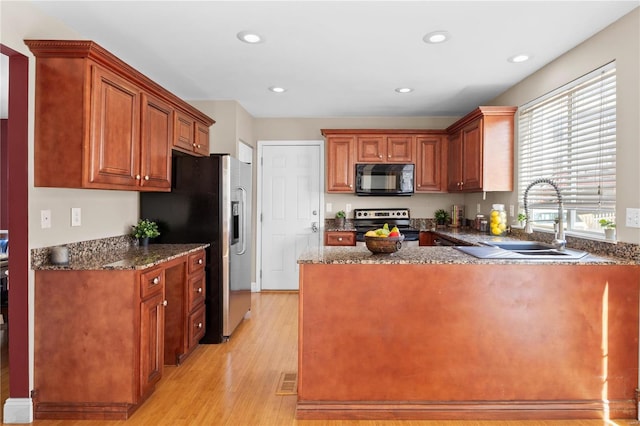 kitchen featuring light wood finished floors, dark stone countertops, appliances with stainless steel finishes, and a sink