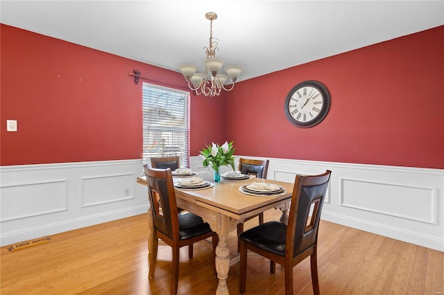 dining area with a notable chandelier, visible vents, wainscoting, and light wood-style floors