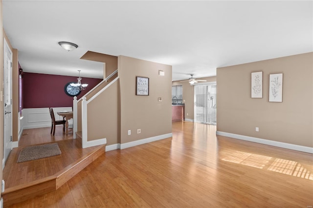 unfurnished living room with baseboards, ceiling fan with notable chandelier, and light wood finished floors