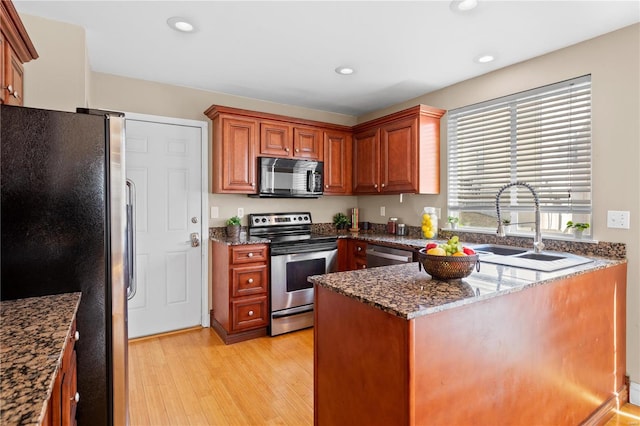 kitchen with light wood-style flooring, a sink, recessed lighting, stainless steel appliances, and dark stone counters